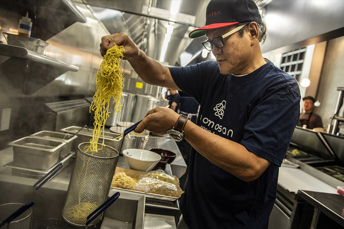 Chef Morimoto in kitchen, pulling cooked noodles out of pot